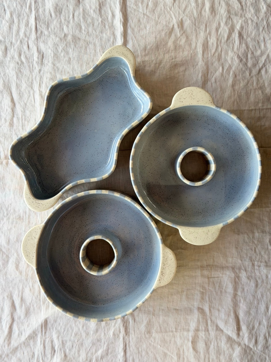 Three handmade blue-striped baking dishes on linen