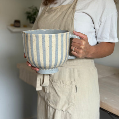 Person holding the large striped mixing bowl by its handle and base.