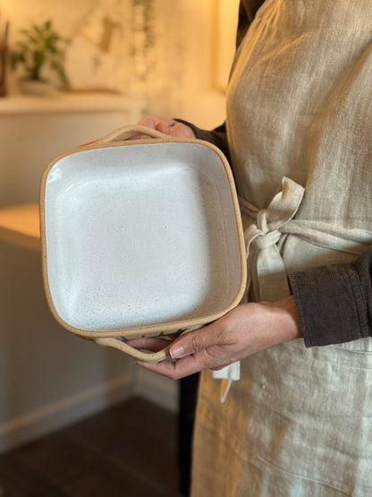 Person holding the small square striped baking dish upright.