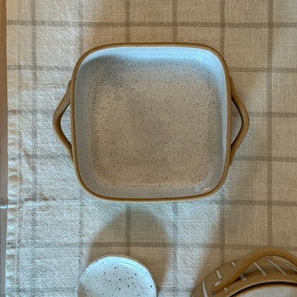 Overhead view of the small square baking dish beside a matching ceramic spoon.