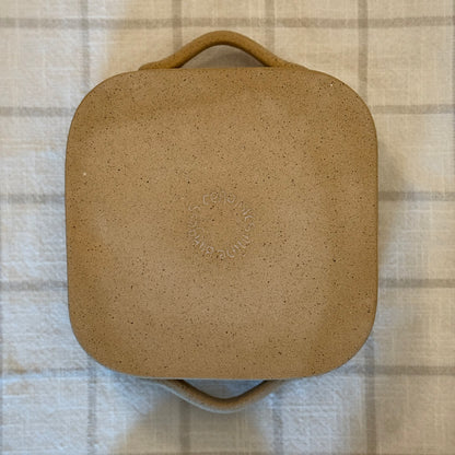 Underside of the small square ceramic dish, showing its unglazed tan base.