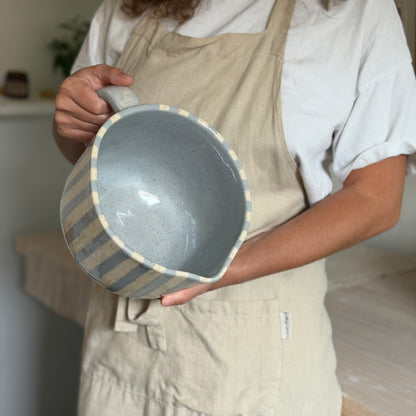 Person tilting the mixing bowl forward to show its blue-gray interior and spout.