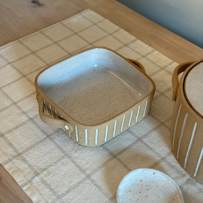 Small square Striora baking dish with white-striped tan sides and two loop handles.