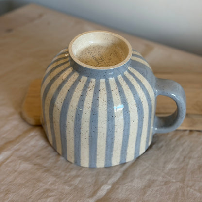 Underside of the striped mixing bowl with a cream foot ring and blue handle.