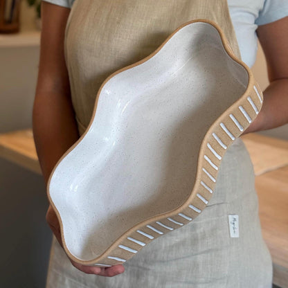 Person holding a long wavy Striora dish with white-striped tan sides and a glazed interior.