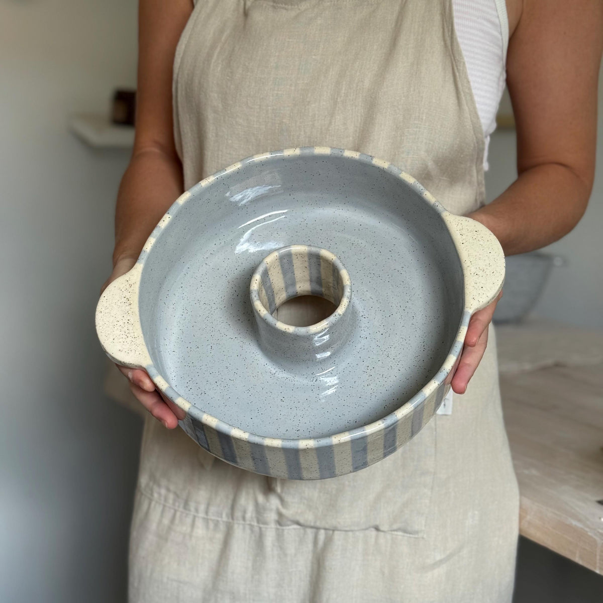 Person holding the striped ceramic bundt pan upright to show its size.