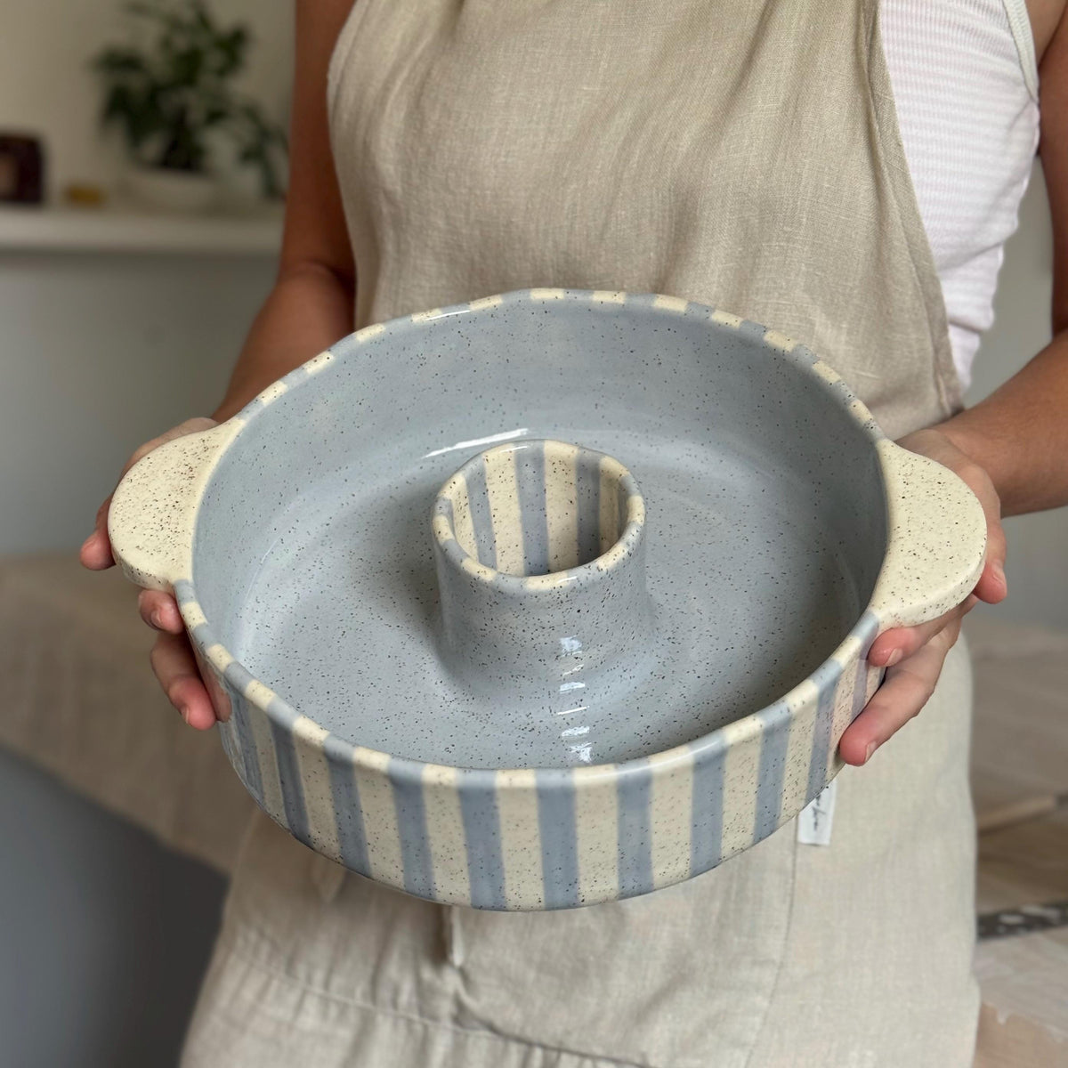 Person holding the ceramic bundt pan level, showing its blue-gray glazed interior.