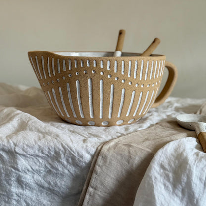 Striped mixing bowl on linen with ceramic spoons inside and its handle at the side.