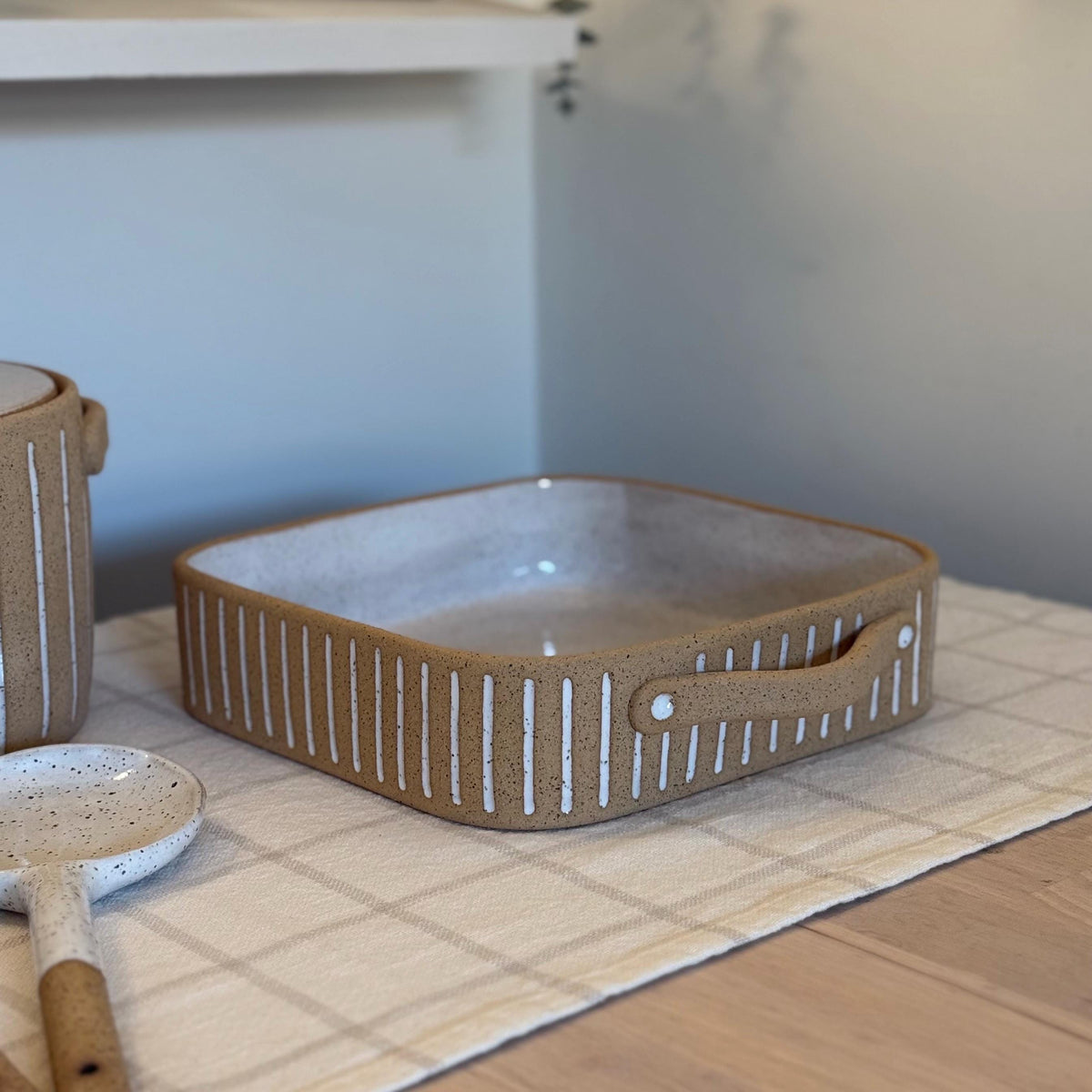 Square Striora baking dish with white-striped tan sides and a speckled white interior.