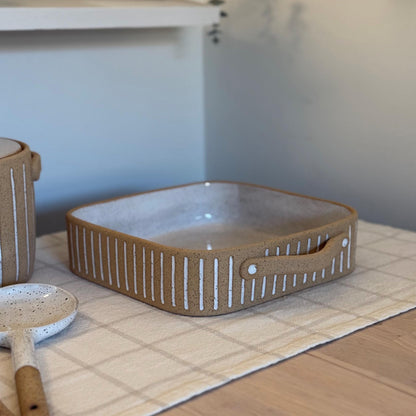 Square Striora baking dish with white-striped tan sides and a speckled white interior.