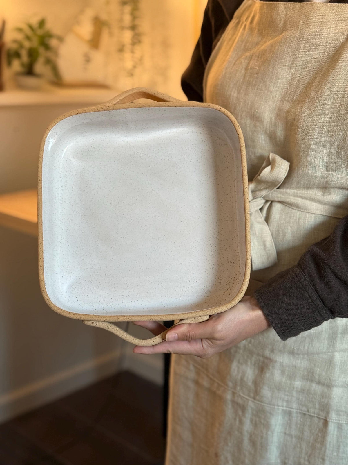 Person holding the square ceramic baking dish upright by its handles.