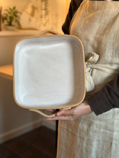 Person holding the square ceramic baking dish upright by its handles.