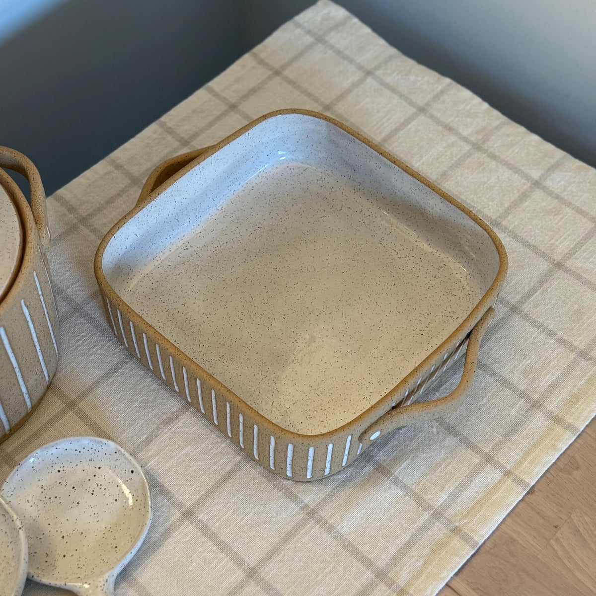 Angled overhead view of the square striped dish beside a matching ceramic spoon.