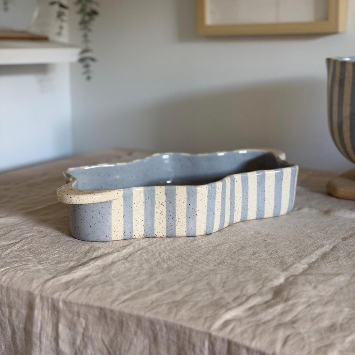 Wide side view of the blue-striped wavy dish on linen.