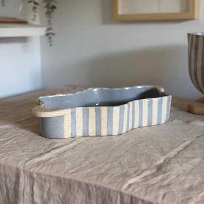 Wide side view of the blue-striped wavy dish on linen.