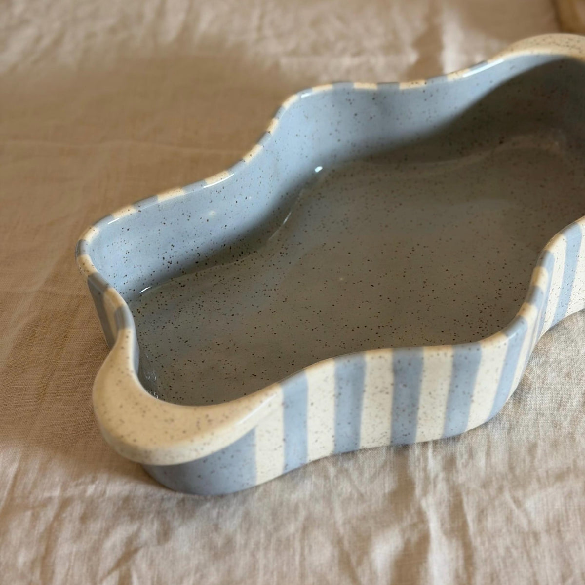 Close angled view of the dish's blue-gray glaze, wavy rim and cream handle.