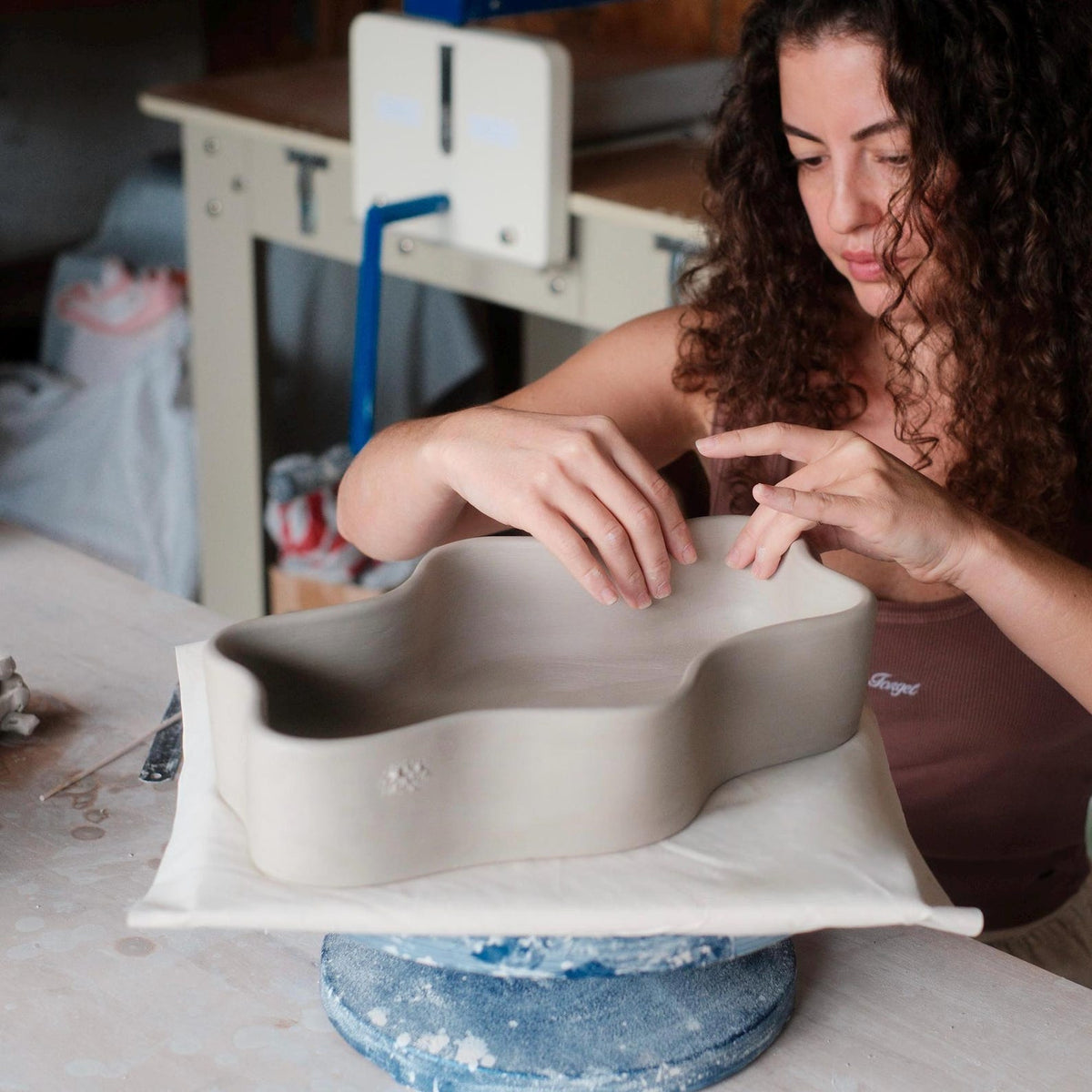 Artist smoothing the rim of an unfired wavy clay dish in the studio.