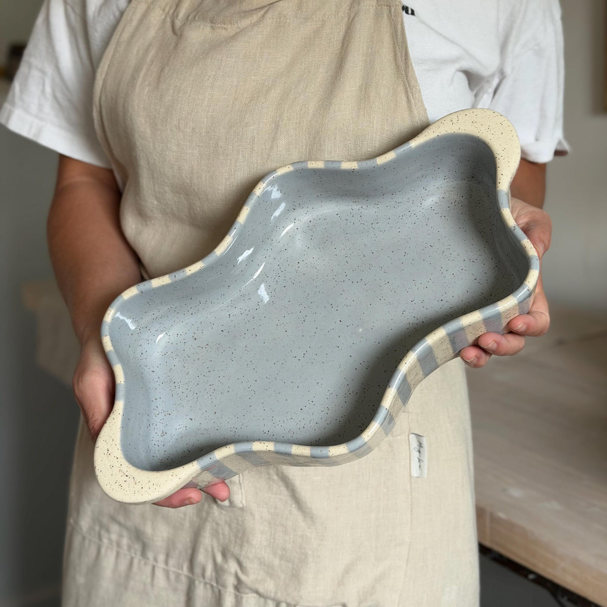 Person holding the blue-striped wavy dish to show its size and blue-gray interior.