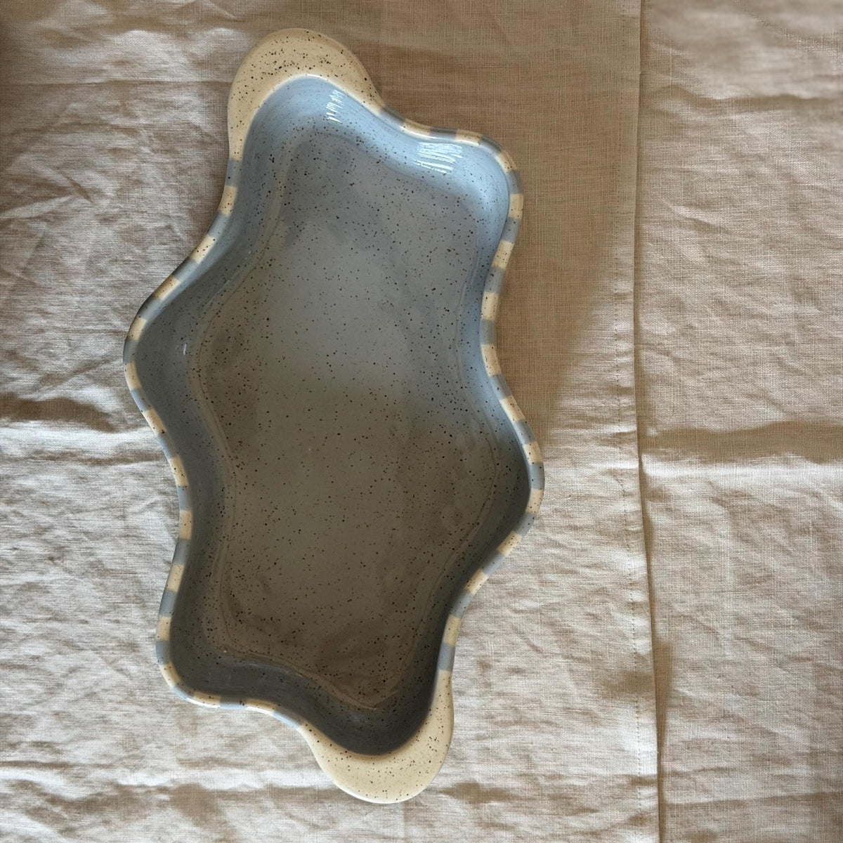 Overhead view of the striped wavy dish with cream handles at either end.