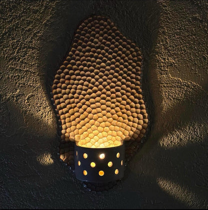Honeycomb wall candle holder illuminated against a dark wall.