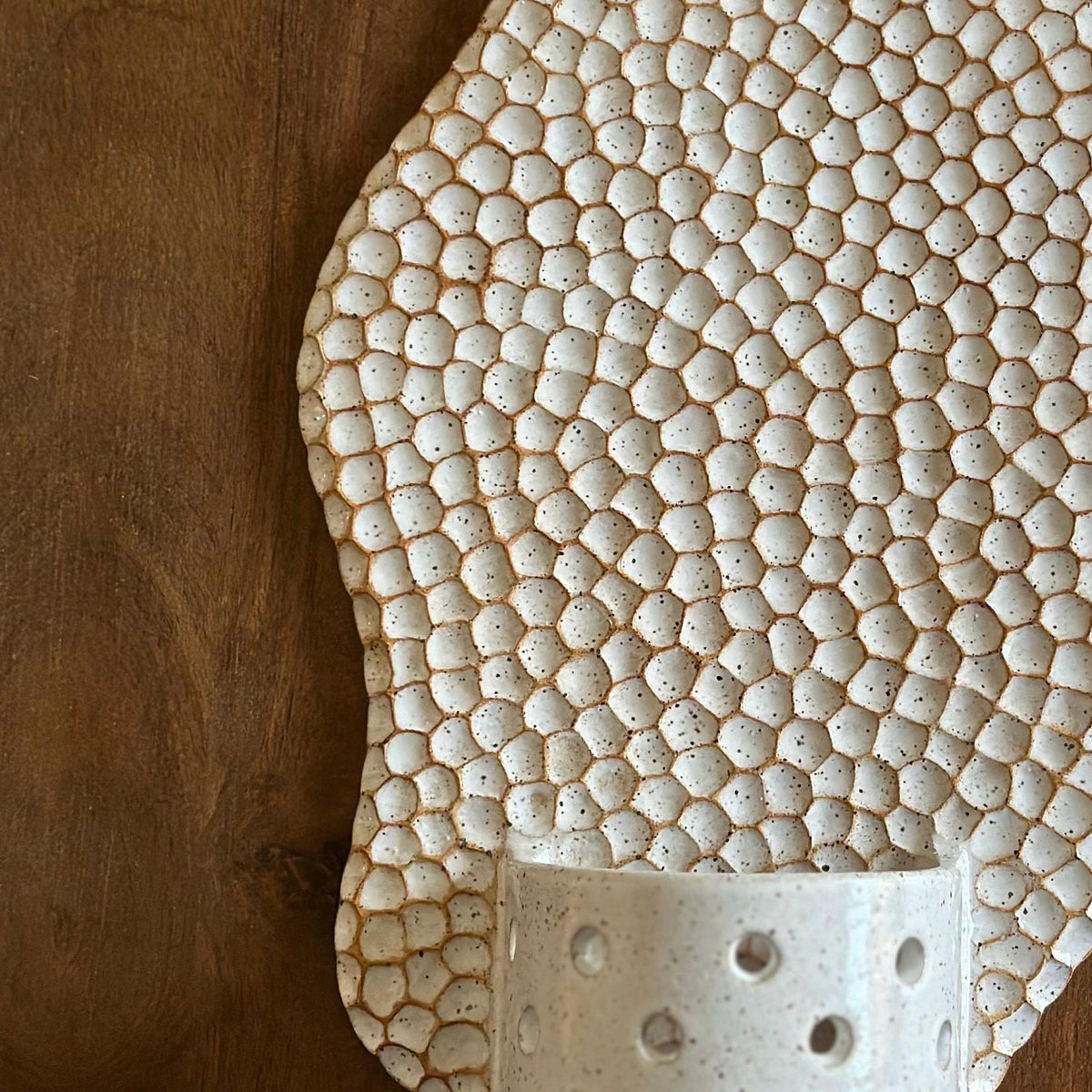 Close view of white glazed honeycomb cells over tan clay beside the candle cup.