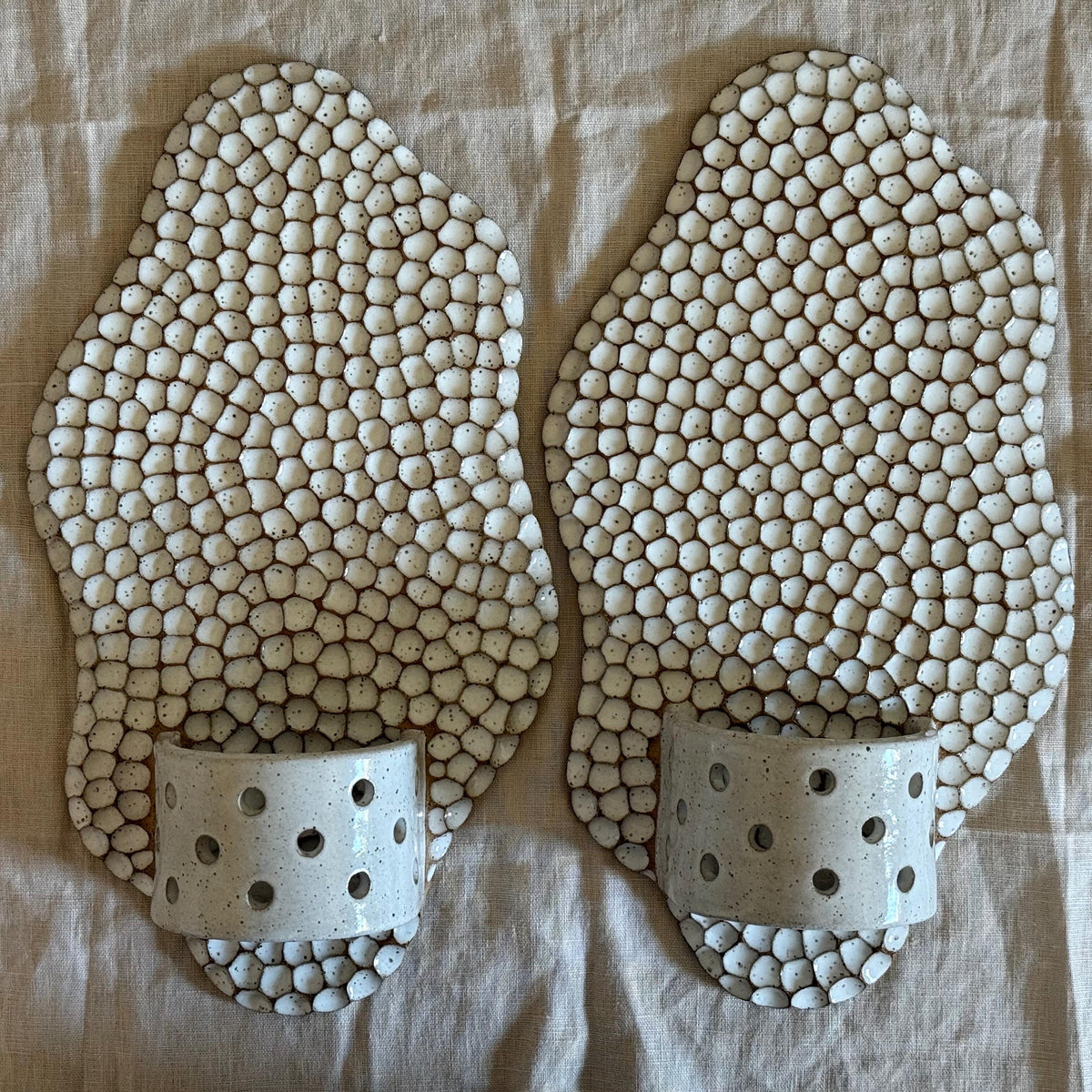 Pair of honeycomb wall candle holders lying on linen.