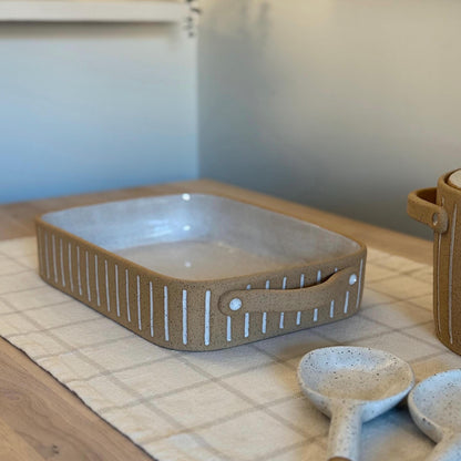 Side view of the rectangular striped baking dish beside matching ceramic spoons.