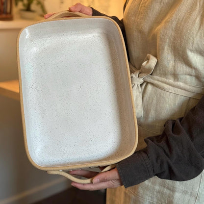 Person holding the rectangular ceramic baking dish upright to show its size and interior.
