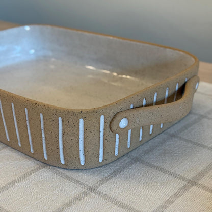 Detail of the rectangular dish's tan loop handle and white carved stripes.
