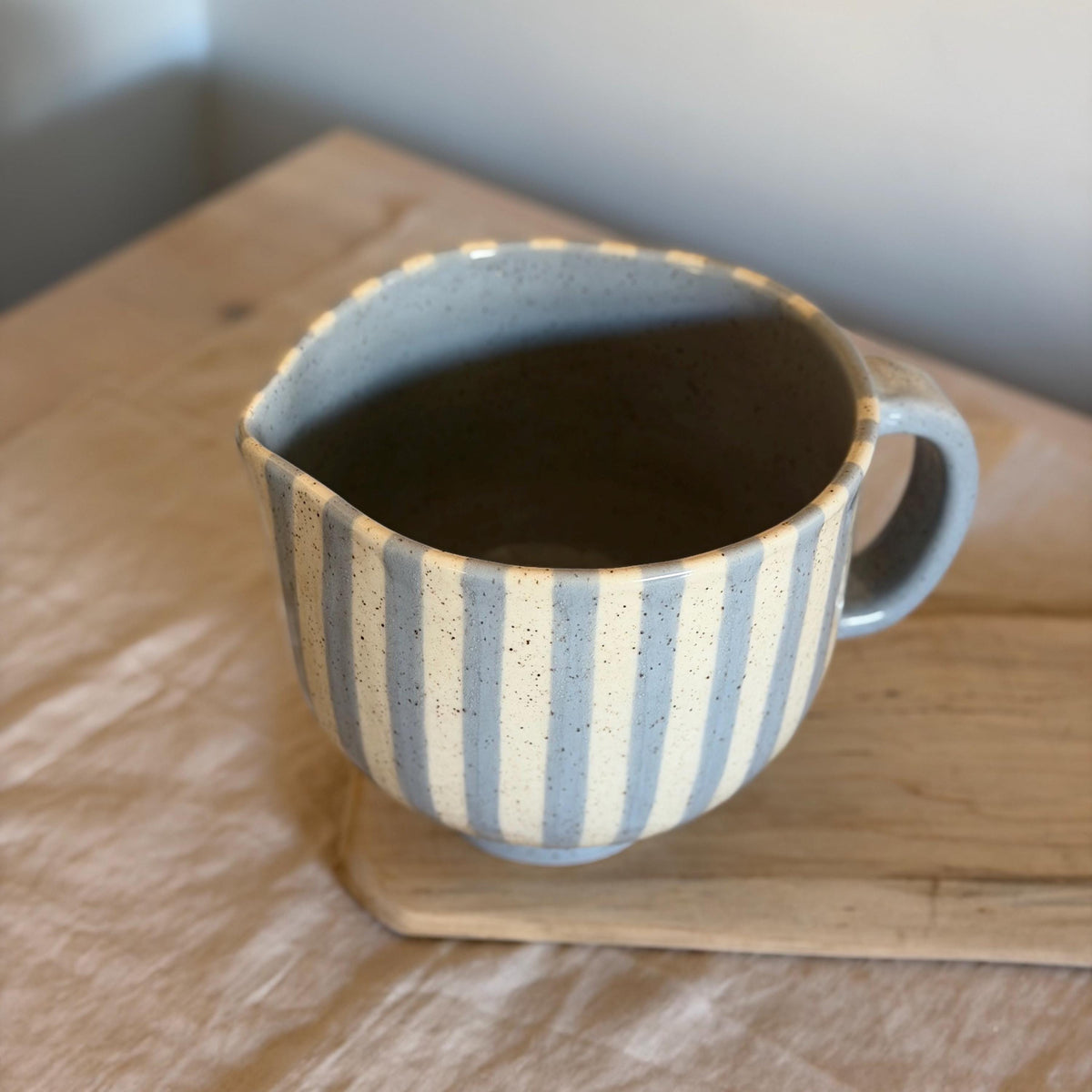 Elevated view of the striped mixing bowl's spout, blue handle and glazed interior.